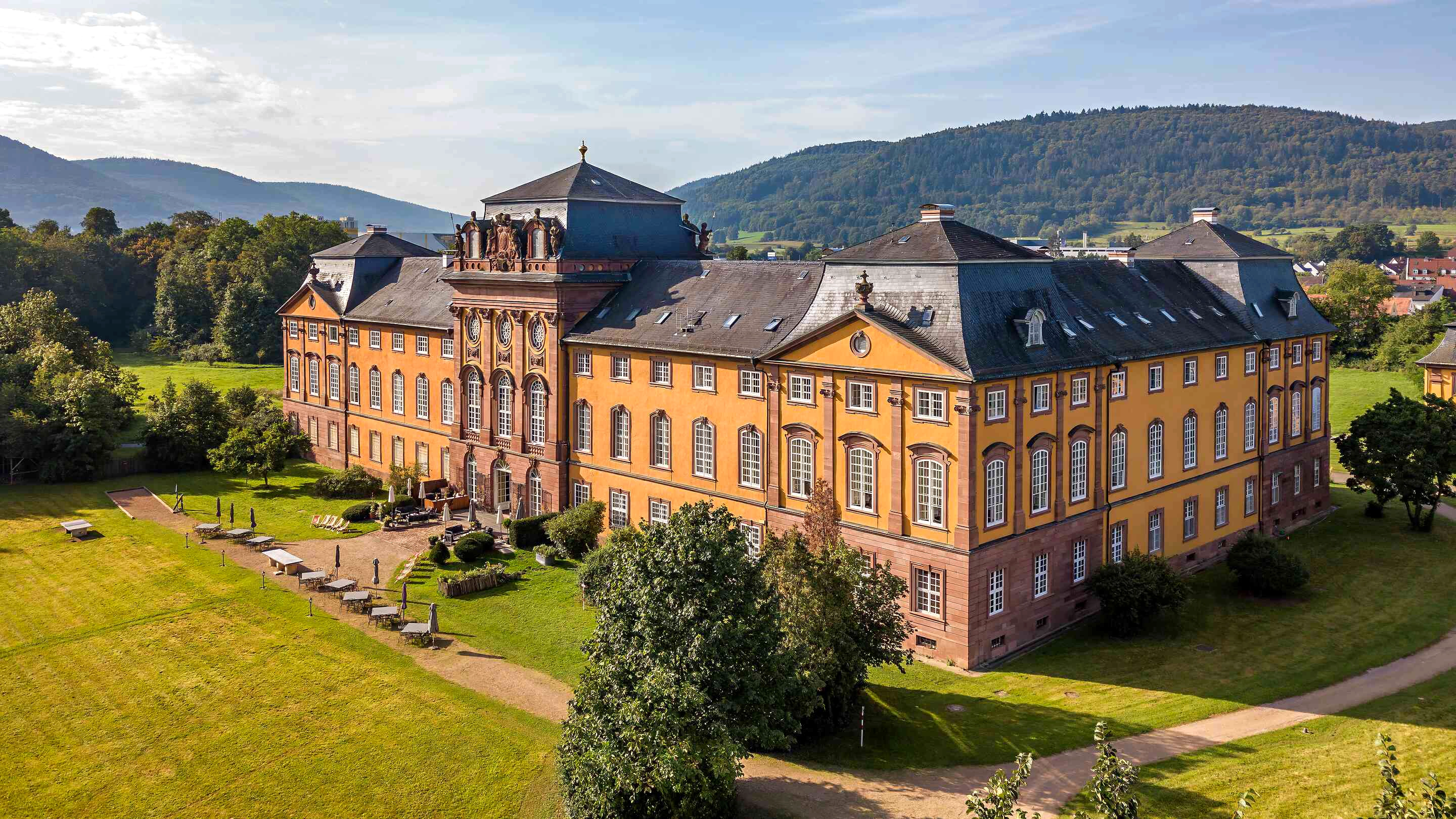 Schloss Löwenstein's ochre Baroque facade overlooking the grounds, with wooded hills behind it.